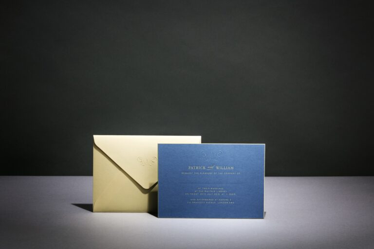Navy engraved invitation with gold lettering beside a gold envelope, Downey Luxury Stationery