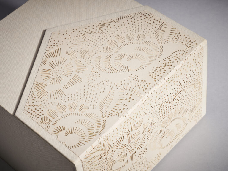 Close view of a cream invitation box wrapped in a laser-cut floral pattern, Downey Luxury Stationery
