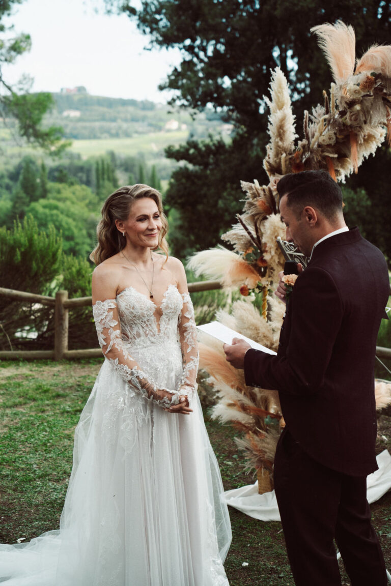 The bride and groom face each other under a pampas grass arch, Tuscan hills behind, Dr Tiziana Di Molfetta