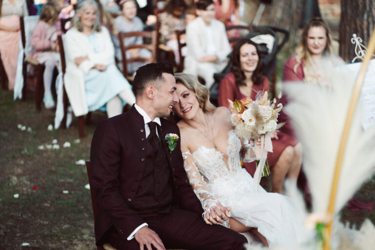 The couple laugh together in their ceremony seats, guests behind, Dr Tiziana Di Molfetta