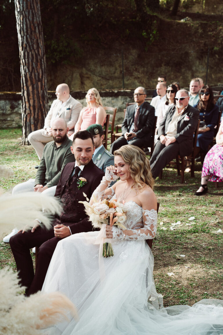 The couple seated during the ceremony among guests and pampas grass, Dr Tiziana Di Molfetta