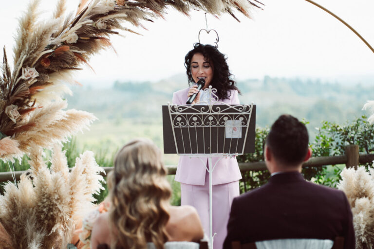 The celebrant addressing the couple from a lectern before the arch, hills beyond, Dr Tiziana Di Molfetta