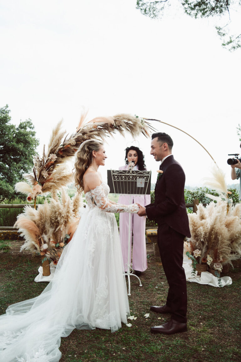 The couple and celebrant beneath the pampas grass arch, Dr Tiziana Di Molfetta