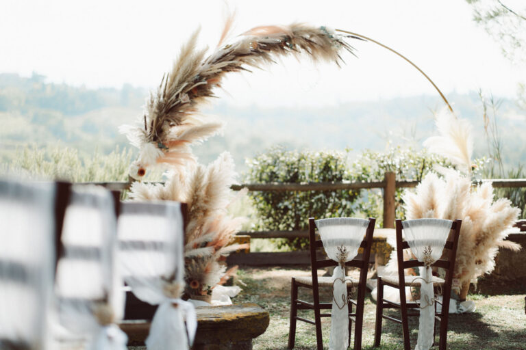 Chairs with ribbon ties and pampas grass beside the arch, Tuscan hills beyond, Dr Tiziana Di Molfetta