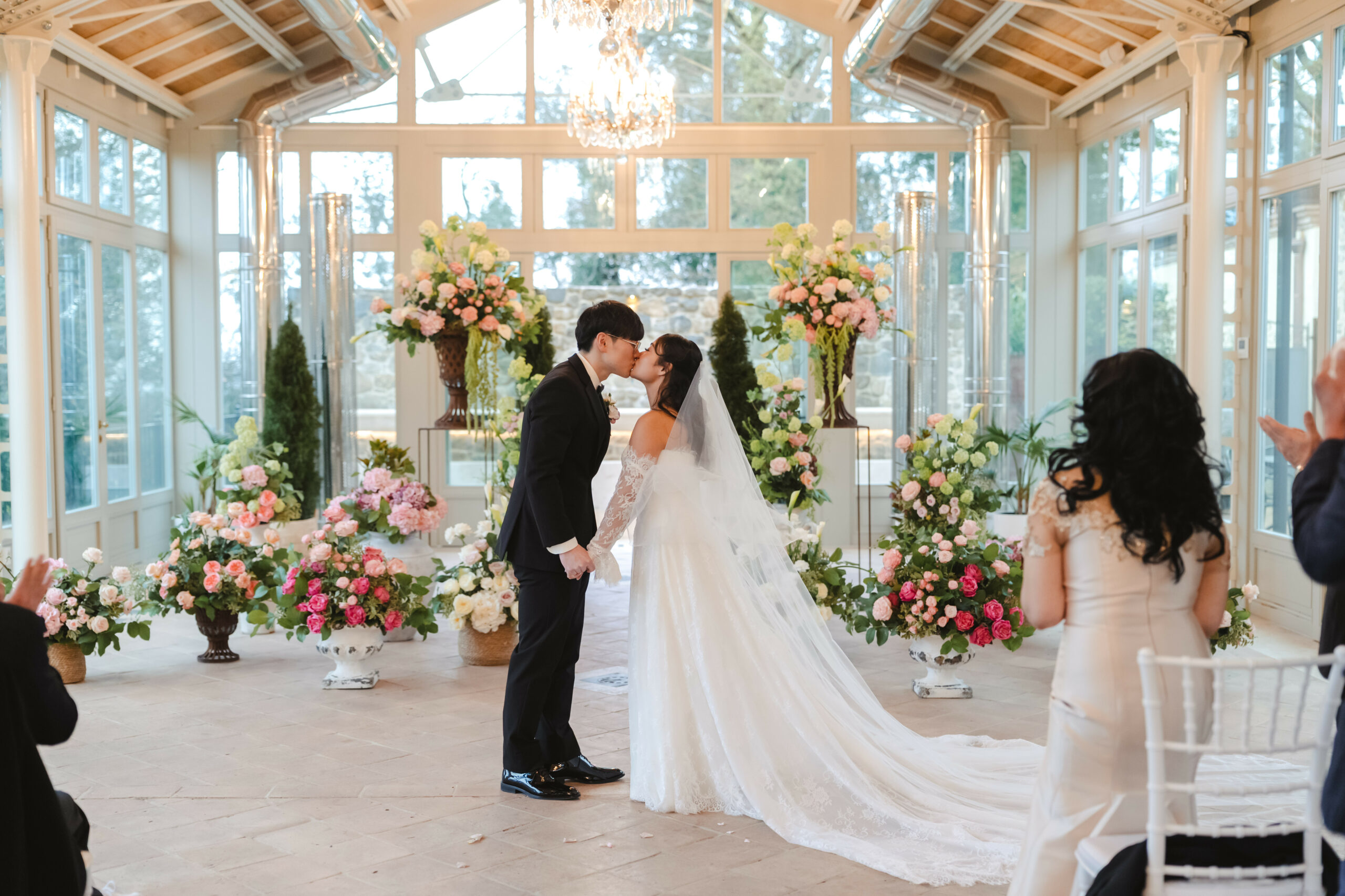 The same glasshouse during the ceremony: the kiss at the end of the flower-lined aisle as guests applaud, Dream On Wedding Team