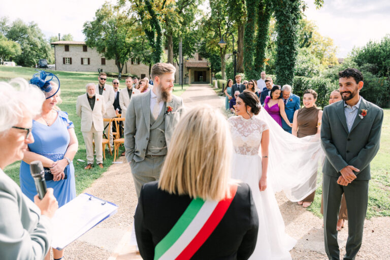 A civil ceremony in a garden: the officiant in the Italian tricolour sash reads to the couple, a farmhouse beyond the trees, Dream On Wedding Team