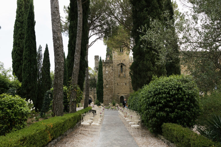 Chairs set along a garden avenue of cypresses leading towards a square stone tower, Dream On Wedding Team