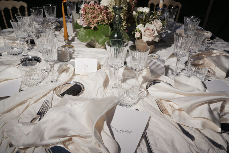 A round table close up: cut crystal glasses, a silk cloth, place cards and a hydrangea and rose centrepiece, Dream On Wedding Team