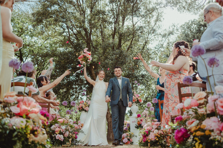 Leaving the ceremony through banks of coral and pink flowers as guests throw petals, Dream On Wedding Team