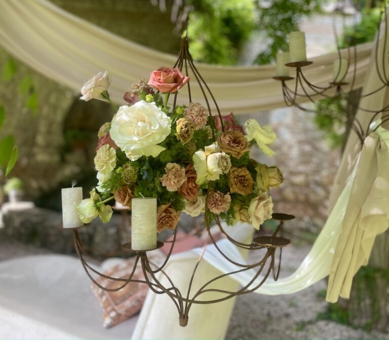 An iron chandelier dressed with garden roses and pillar candles, cream drapes behind, Dream On Wedding Team