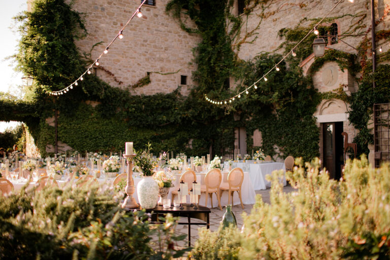 A walled courtyard laid for dinner under festoon lights, an ivy-covered stone building behind, Dream On Wedding Team