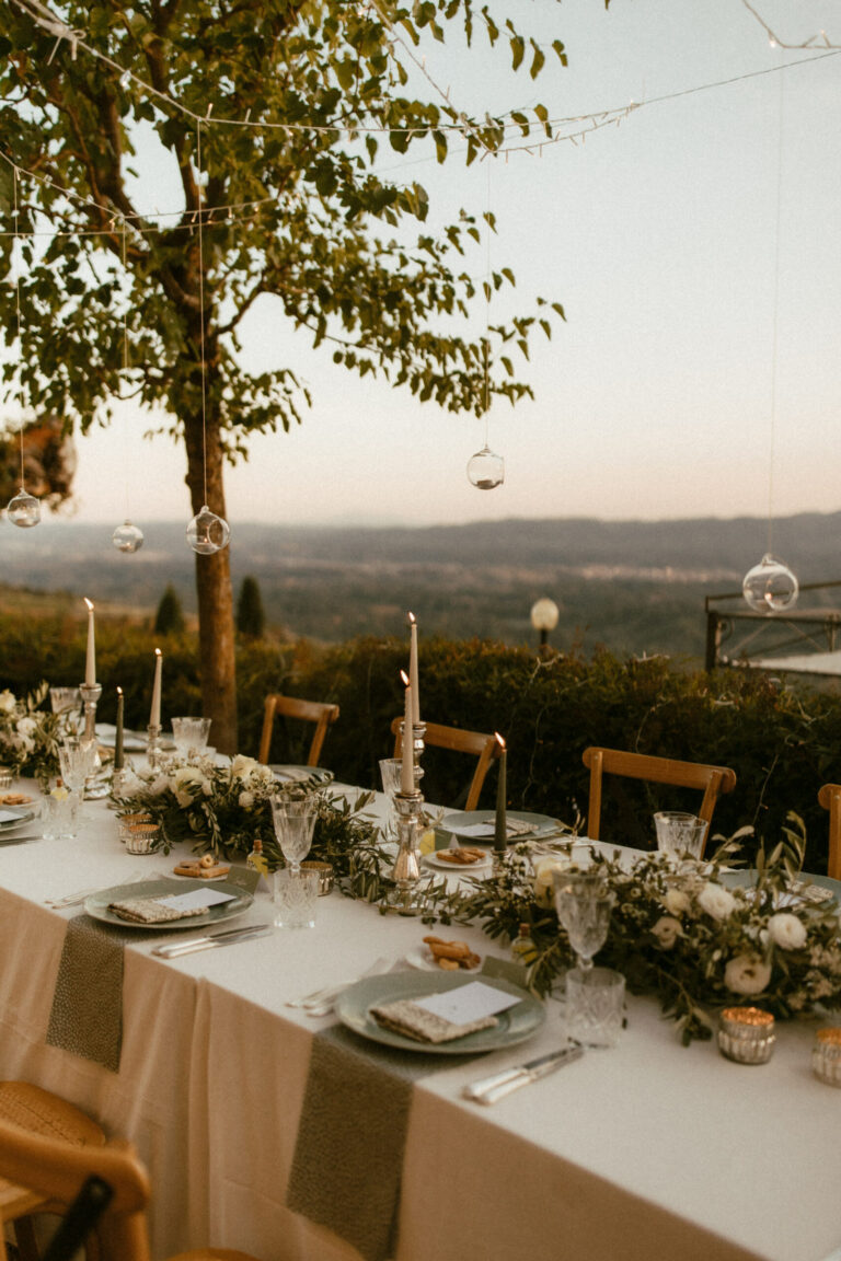 A dinner table on the edge of a terrace, tapers and greenery down the centre, hills fading into the distance, Dream On Wedding Team