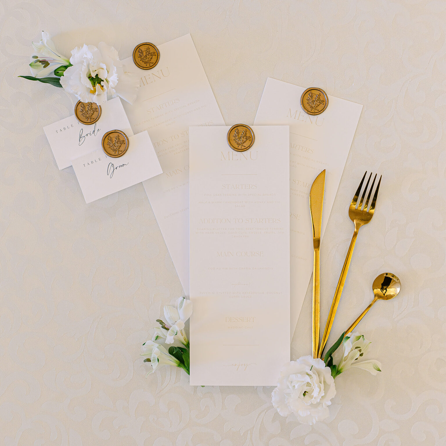 Menu cards with gold wax seals and cutlery on cream linen