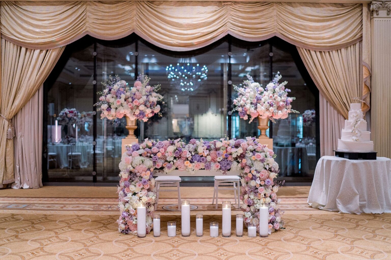 A flower-banked sweetheart table and cake on a draped stage