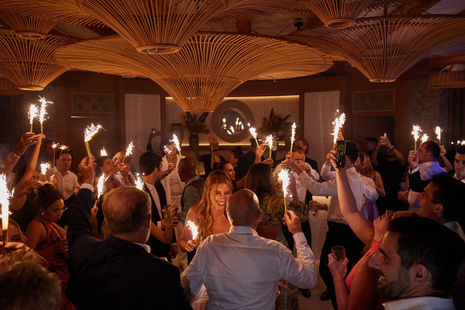 Guests holding sparklers in a dining room under a woven ceiling at night, Dream Weddings Mykonos