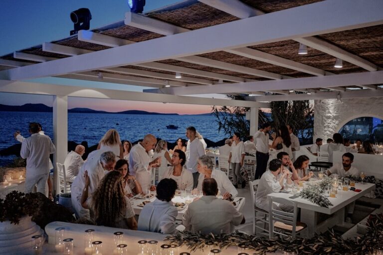 Guests seated at long tables beneath a white pergola above the sea at dusk, Dream Weddings Mykonos