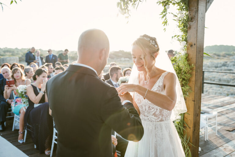 Ring exchange at an outdoor ceremony under a wooden pergola near the coast, DS Studiofotografico