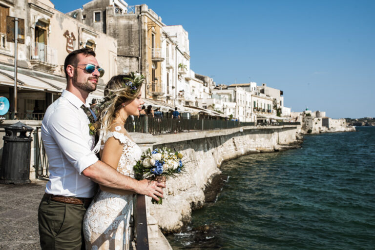 Couple on a seafront promenade below the old town, bouquet in hand, DS Studiofotografico