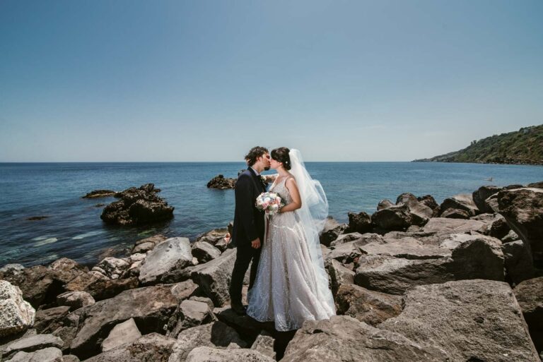 Couple kissing on the rocks at the water's edge, DS Studiofotografico