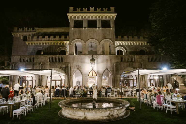 Reception tables on the lawn in front of a castellated villa at night, DS Studiofotografico