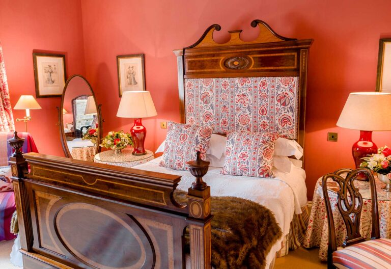 A bedroom with red walls, an inlaid wooden bed and a floral headboard, Dundas Castle