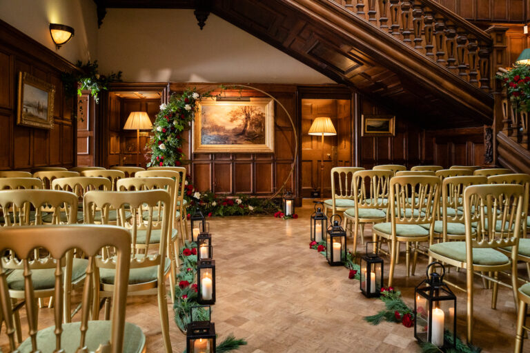 The panelled Main Hall at the foot of the grand staircase, set with gold chairs, lanterns and festive greenery for a ceremony, Dundas Castle
