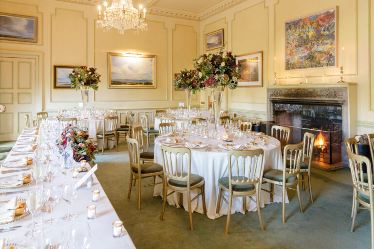 The Croquet Room laid for dinner, with a crystal chandelier, open fire and round tables, Dundas Castle