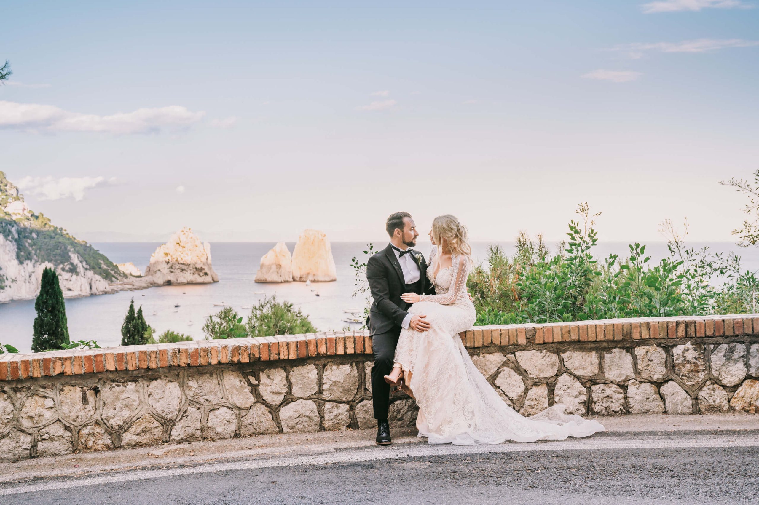 The couple on a stone wall above the sea at golden hour, sea stacks offshore, southern Italian coast, Elisa Prati Wedding Italy
