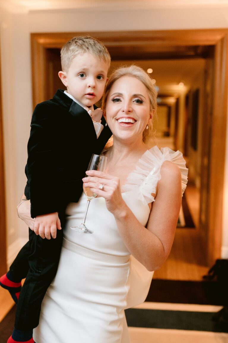 A bride carrying a young boy in black tie, champagne in hand, Corinthia London, Elizabeth Hsieh Make Up Artist