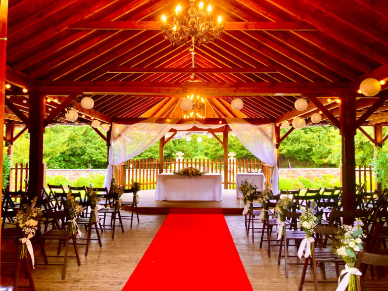 A red carpet aisle under the timber roof of the Italian Garden veranda, with chandeliers and paper lanterns, Elmhay Park