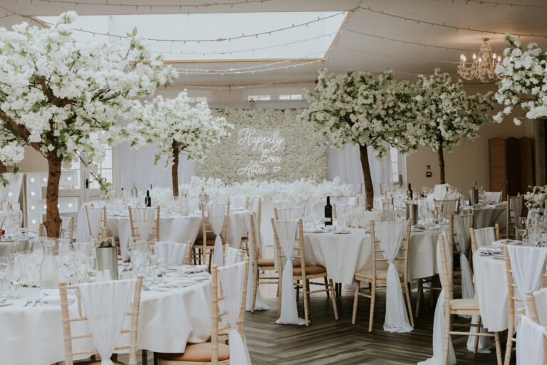 The Orangery styled with white blossom trees and a flower wall behind the top table, Elmhay Park