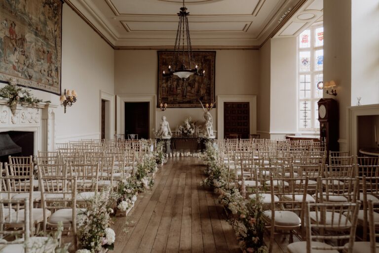 The main house set for a ceremony, chairs in rows beneath a tapestry and chandelier, Elmore Court