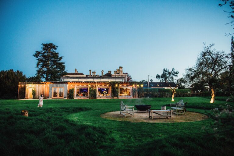 The Gillyflower lit at dusk, a fire pit burning on the lawn, Elmore Court