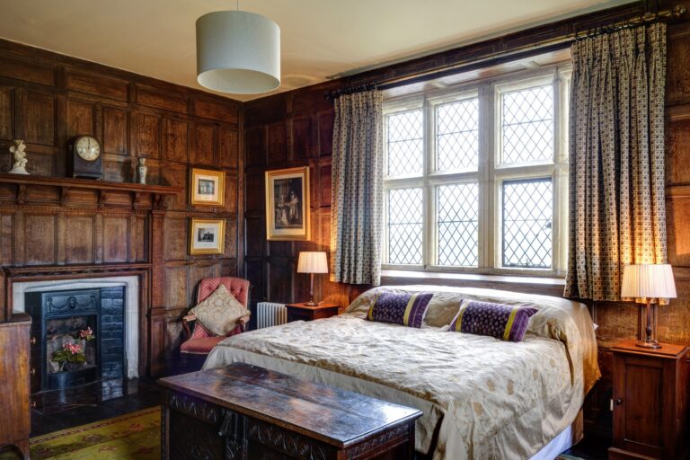 A wood-panelled bedroom with a grand bed and leaded windows, Elmore Court