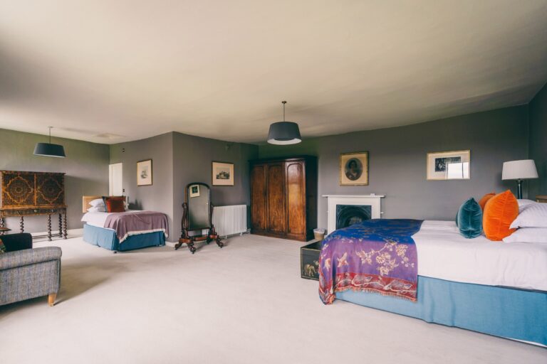 A bedroom with painted panelling, a fireplace and a scatter of art, Elmore Court