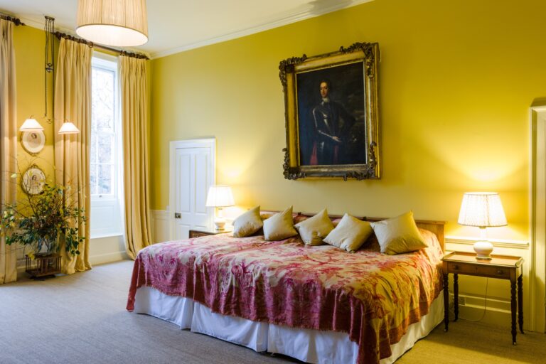 A yellow bedroom with a gilt-framed portrait above a grand bed, Elmore Court