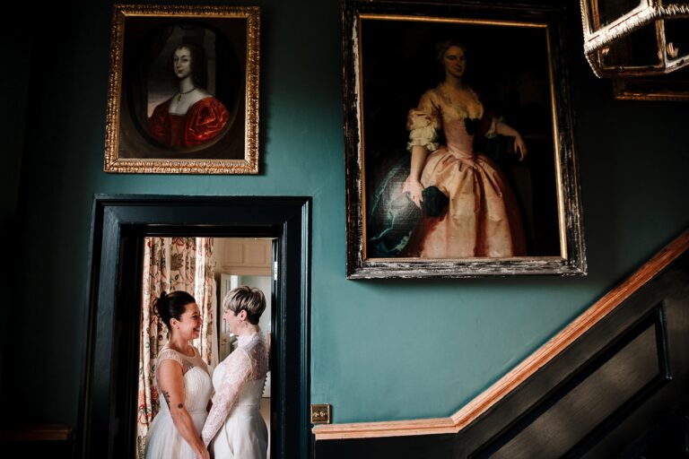 A couple embracing in a blue room hung with portraits, Elmore Court