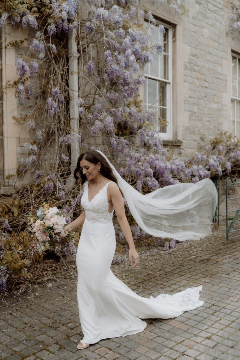 A bride, her veil catching the light, by a blossoming wall, Elmore Court