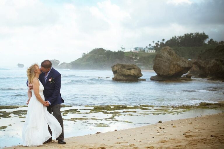 A bride and groom embracing on the rocky east coast shore with large boulders and mist behind, Elope Barbados