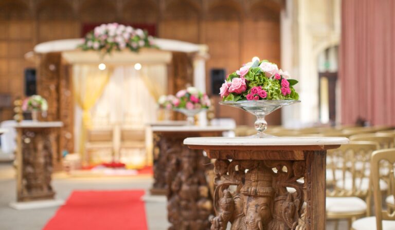 A carved wooden mandap set for a Hindu ceremony in the Great Hall, a red aisle between the flowers, Eltham Palace