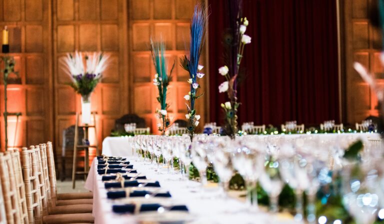 A long banquet table in the Great Hall, peacock feathers and low greenery among the glassware, Eltham Palace