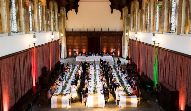 The Great Hall banquet seen from the minstrels' gallery, warm uplighting on the panelled screen, Eltham Palace