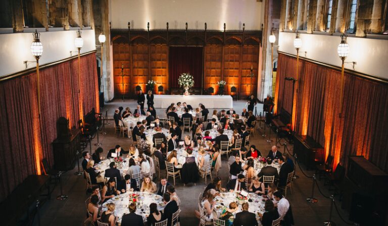 The Great Hall reception from above, round tables and a floral top table under amber light, Eltham Palace