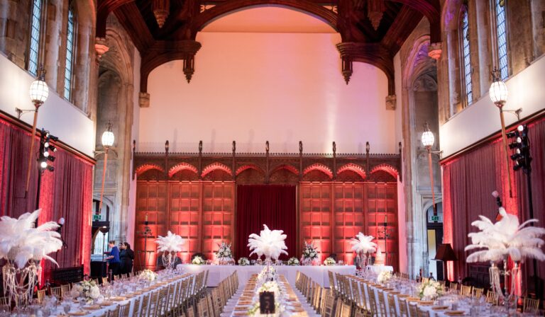 The Great Hall laid for a red-themed banquet, ostrich feathers and floor uplighting against the panelling, Eltham Palace