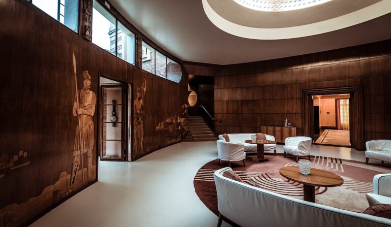 The Entrance Hall furnished as a lounge, marquetry figures above curved sofas and the sweep of the stair, Eltham Palace