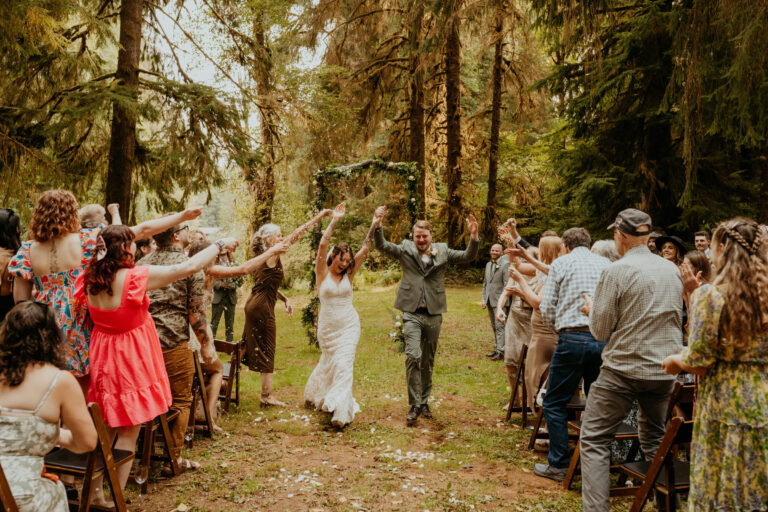 Guests with arms raised beneath tall trees at a forest wedding ceremony, Emett Joseph Photography