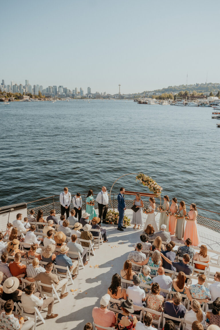 Waterfront ceremony seen from above, guests seated in curved rows facing the water, Emett Joseph Photography