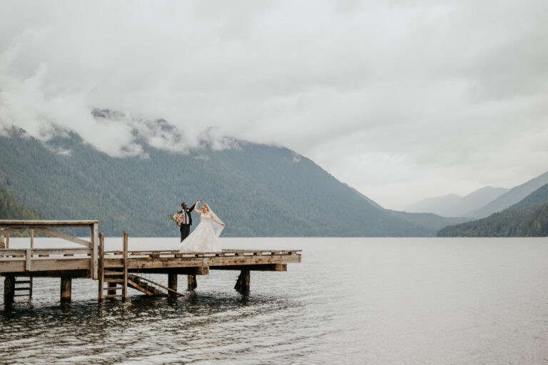 Couple at the end of a lake dock beneath cloud-covered mountains, Lake Crescent, Emett Joseph Photography