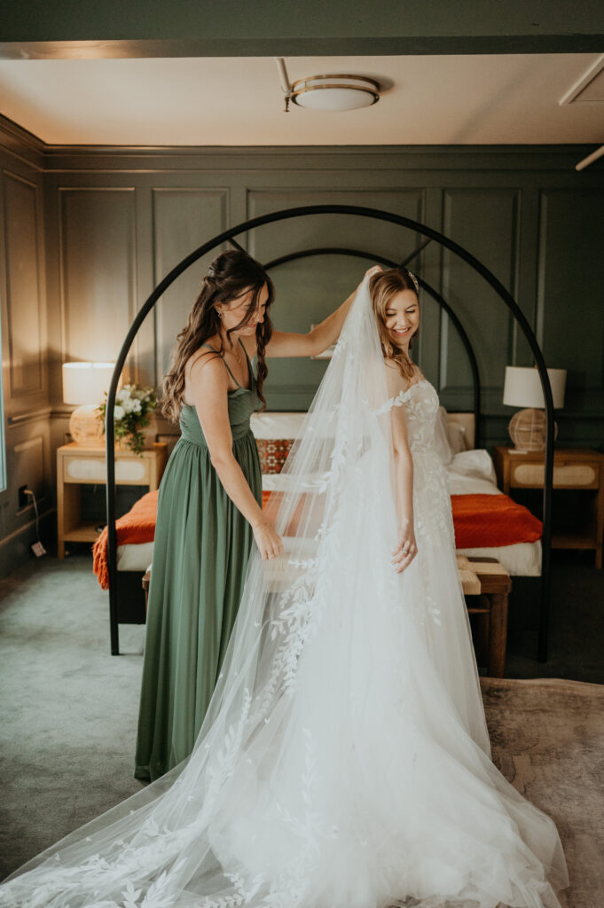 Bride in a long veil with a bridesmaid in green, in an arched doorway, Emett Joseph Photography