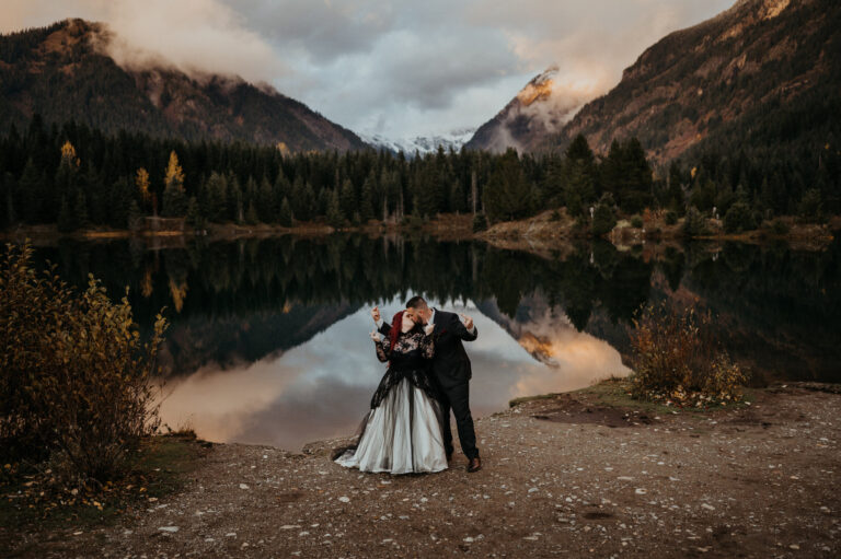 Couple at the edge of a mountain lake at dusk, peaks reflected in the water, Emett Joseph Photography